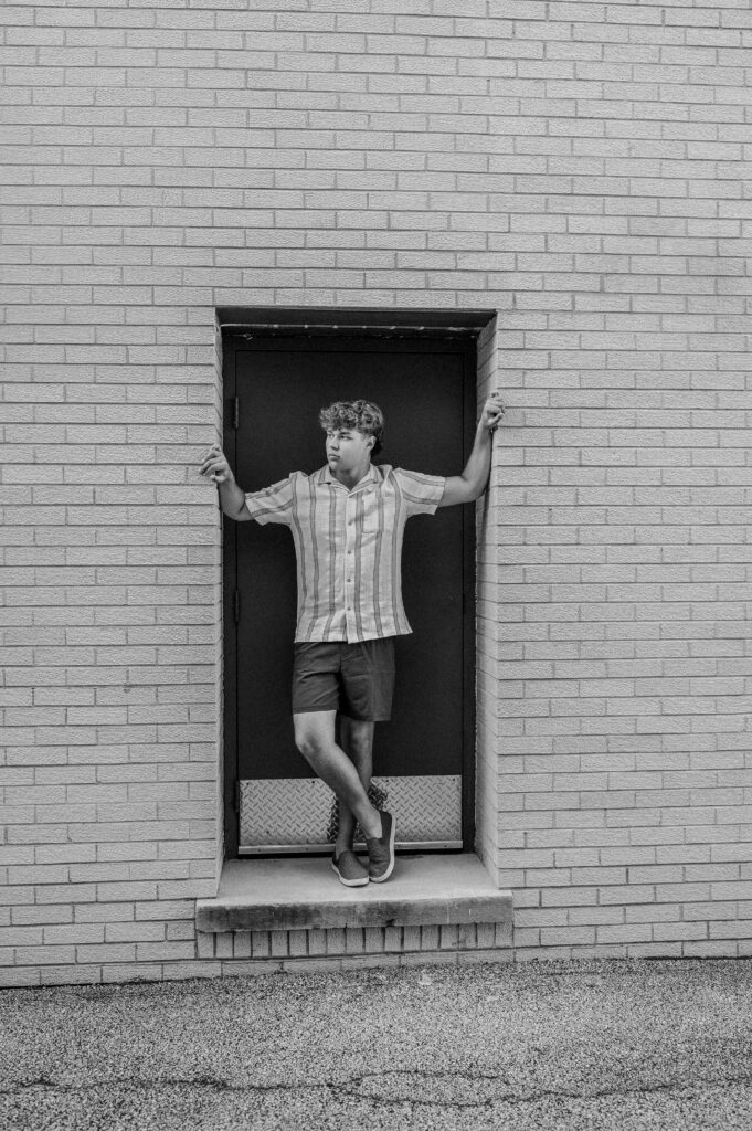Black and white senior portrait of a boy in a striped shirt posed in a brick doorway — urban downtown senior pictures near Barrington IL