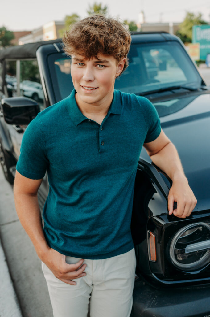 Senior boy in a teal polo leaning against a black Ford Bronco in an urban setting — personalized senior pictures in the Chicago northwest suburbs